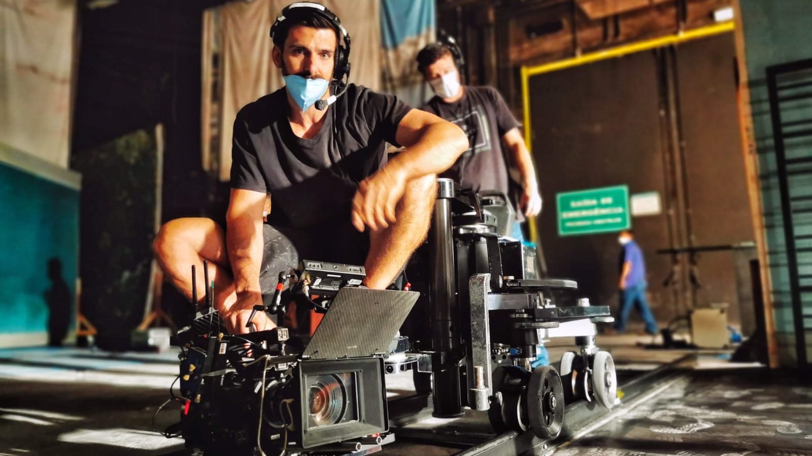 Pedro agachado en el dolly sobre rieles, con la cámara y el matte box, en estudio, en Cara e Coragem