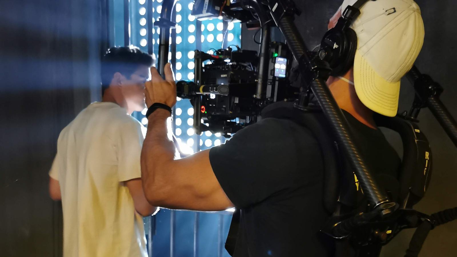 Pedro operando en gimbal junto al actor, en decorado oscuro con paneles de luz, en Um Lugar ao Sol